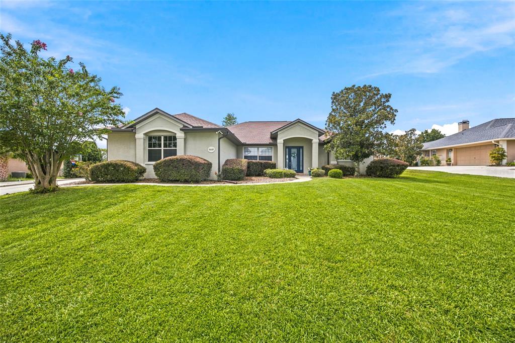 A single-story house with a green lawn, landscaping, and a blue front door — 9640 SE 61 TERRACE, BELLEVIEW, FL