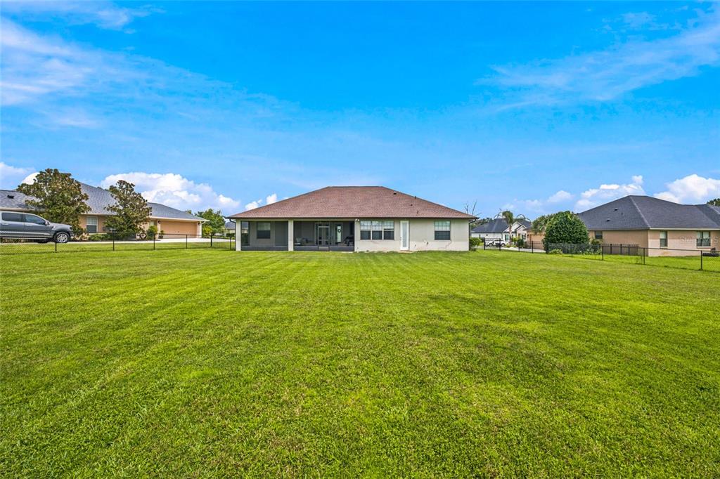 The backyard of a single-story house features a large lawn and a covered patio — 9640 SE 61 TERRACE, BELLEVIEW, FL