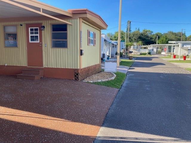 A light yellow mobile home with a brown door and carport sits beside a road — 800 32ND AVENUE S UNIT 227, ST PETERSBURG, FL