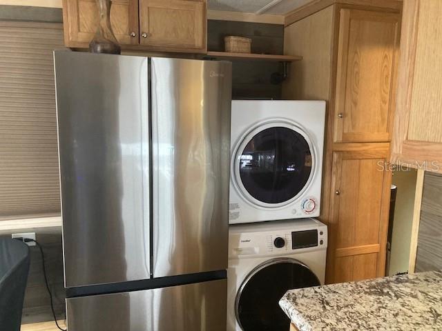 A stainless steel refrigerator stands next to a stacked washer and dryer in a kitchen — 800 32ND AVENUE S UNIT 227, ST PETERSBURG, FL