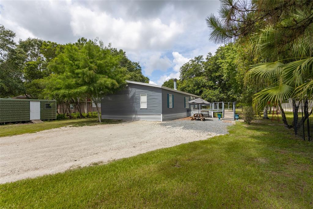 A gray mobile home sits on a gravel lot surrounded by trees and green grass — 1013 FOREST PARK STREET, BUNNELL, FL