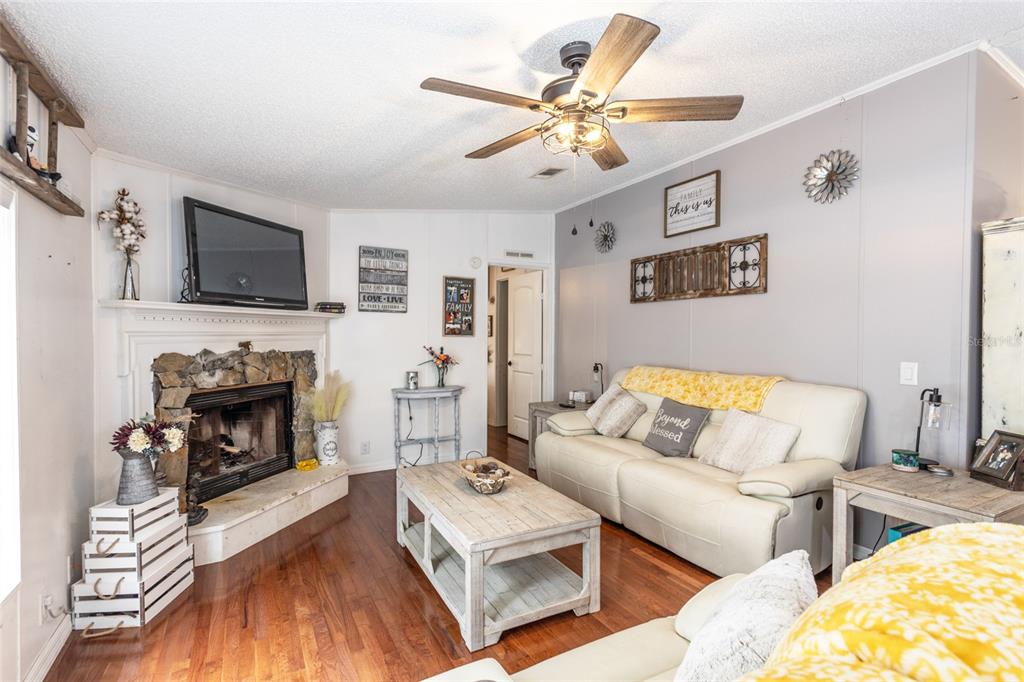 A living room features a stone fireplace, wood floors, a ceiling fan, and white sofas — 1013 FOREST PARK STREET, BUNNELL, FL