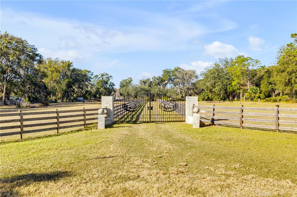 A metal gate with decorative deer silhouettes stands between two stone pillars and wooden fencing — 420 ROBERTS ROAD, PIERSON, FL