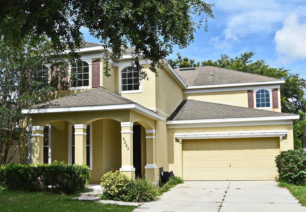 A two-story yellow stucco house features a covered front porch, a two-car garage, and arched windows — 9223 LEELAND ARCHER BOULEVARD, ORLANDO, FL