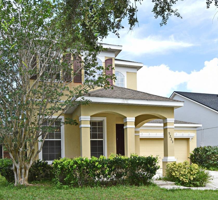 A two-story yellow stucco house features a covered front porch and an attached garage — 9223 LEELAND ARCHER BOULEVARD, ORLANDO, FL