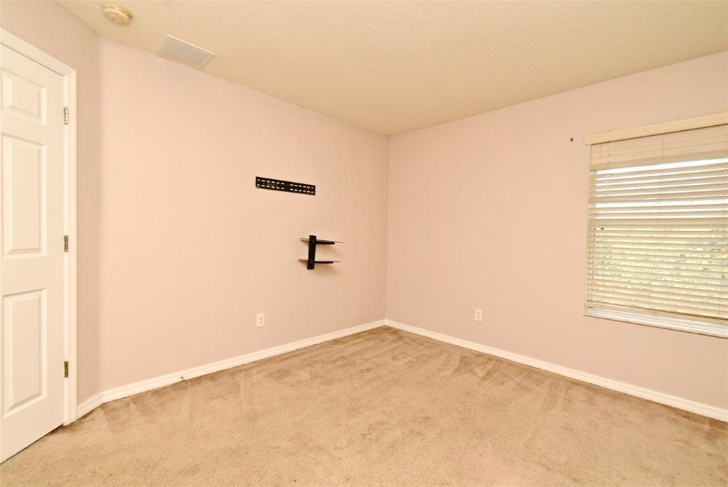 An empty bedroom features beige carpet, light-colored walls, a window with blinds, and wall-mounted brackets — 9223 LEELAND ARCHER BOULEVARD, ORLANDO, FL