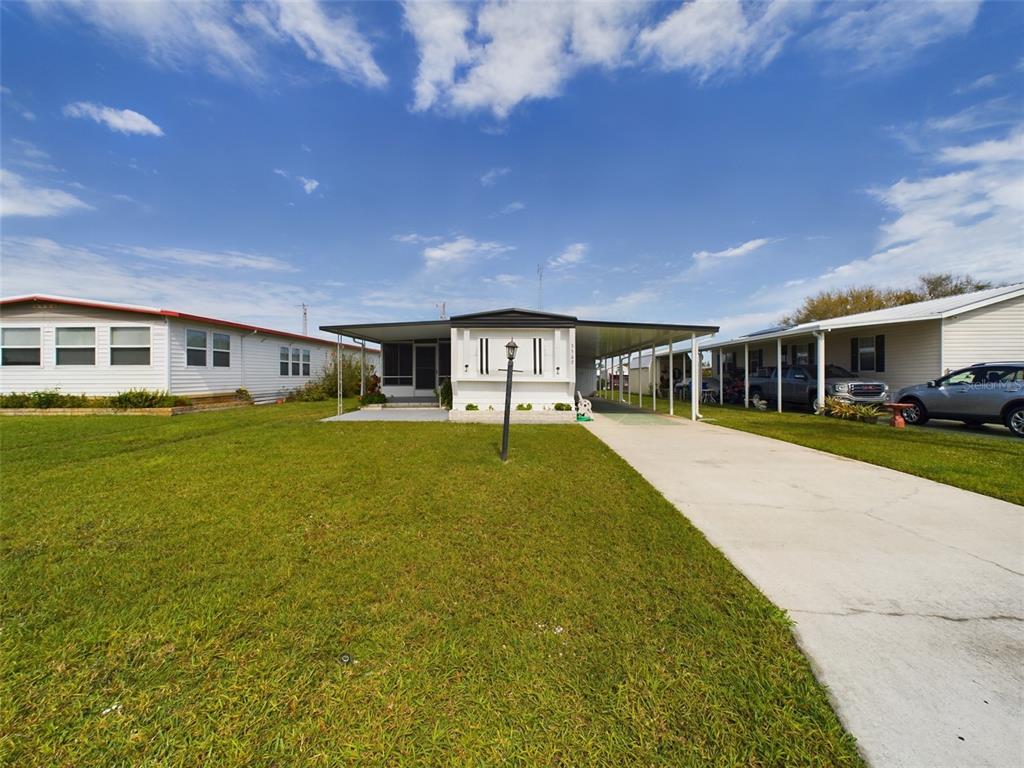 A single-story mobile home with a carport and a concrete driveway under a blue sky — 3502 DELAWARE AVENUE, SEBRING, FL