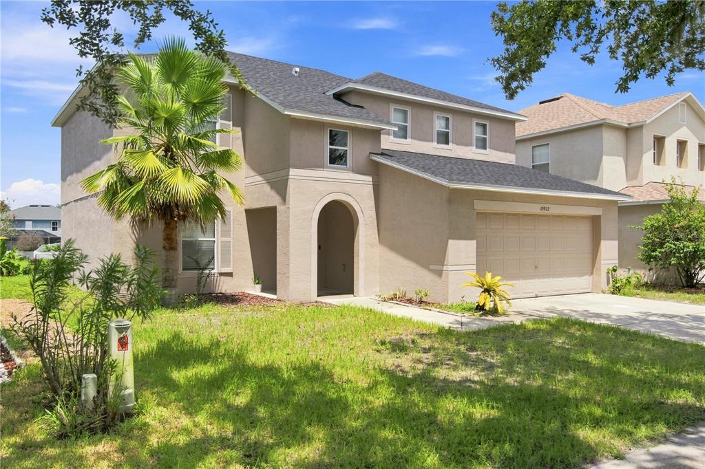 A two-story beige stucco house features a palm tree, a front porch, and a garage — 10922 SUBTLE TRAIL DRIVE, RIVERVIEW, FL