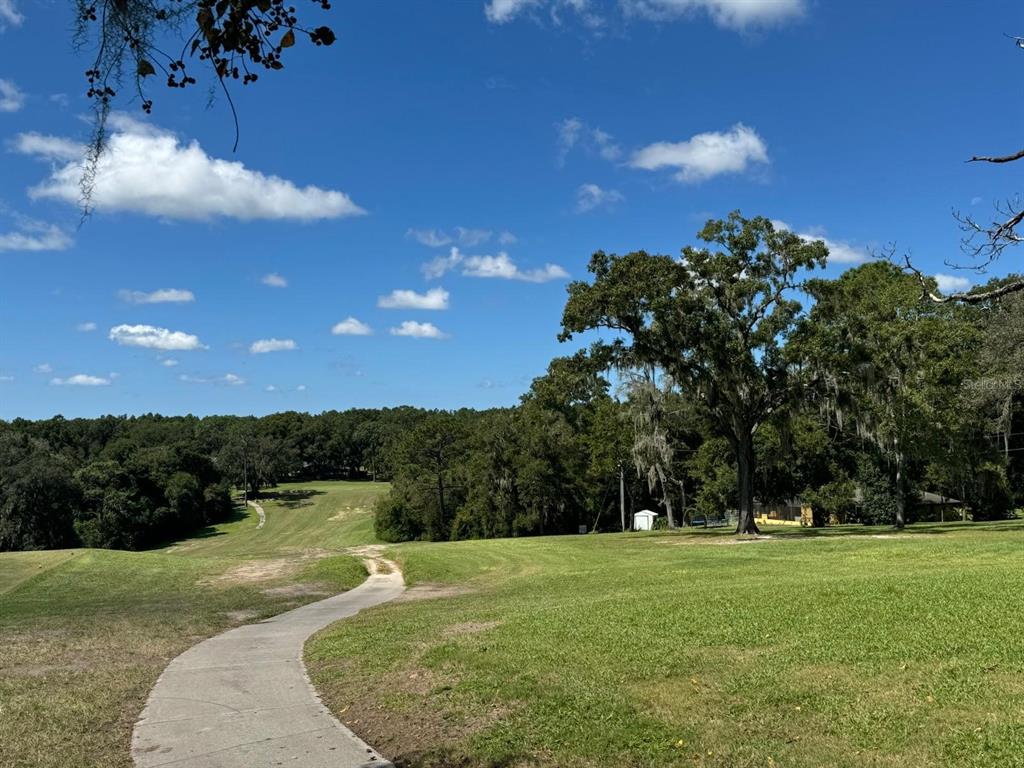 A concrete path winds through a grassy golf course toward a line of trees — 297 W WHITMARSH COURT, CITRUS SPRINGS, FL