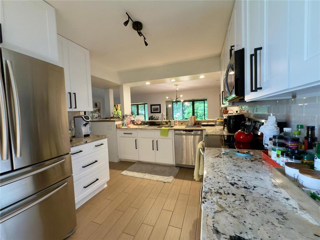 A kitchen features white cabinets, stainless steel appliances, granite countertops, and light wood-look tile flooring — 8113 BREEZE COVE LANE, ORLANDO, FL