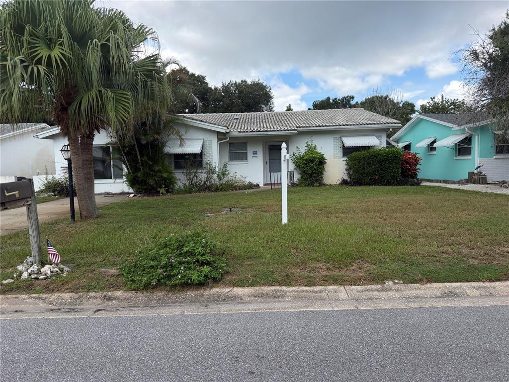 A single-story white house with a tiled roof sits behind a lawn and palm tree — 29768 67TH STREET N, CLEARWATER, FL