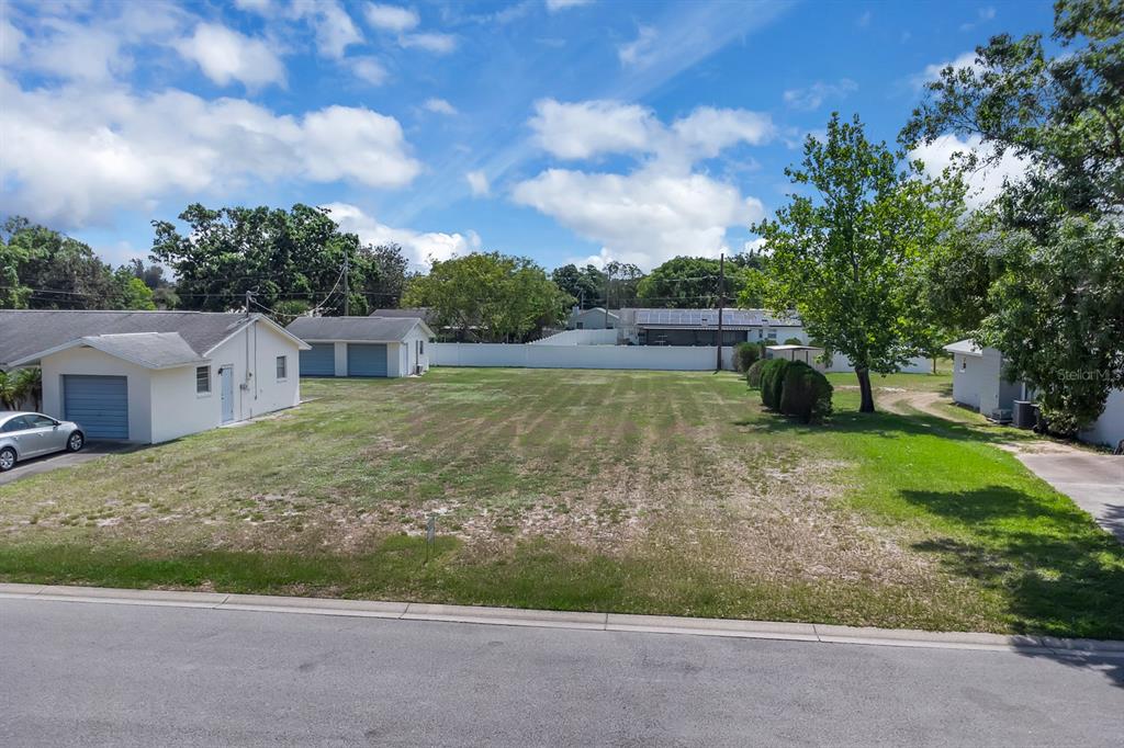 An empty residential lot sits between two houses under a blue sky with clouds — DELAWARE AVENUE, ST CLOUD, FL