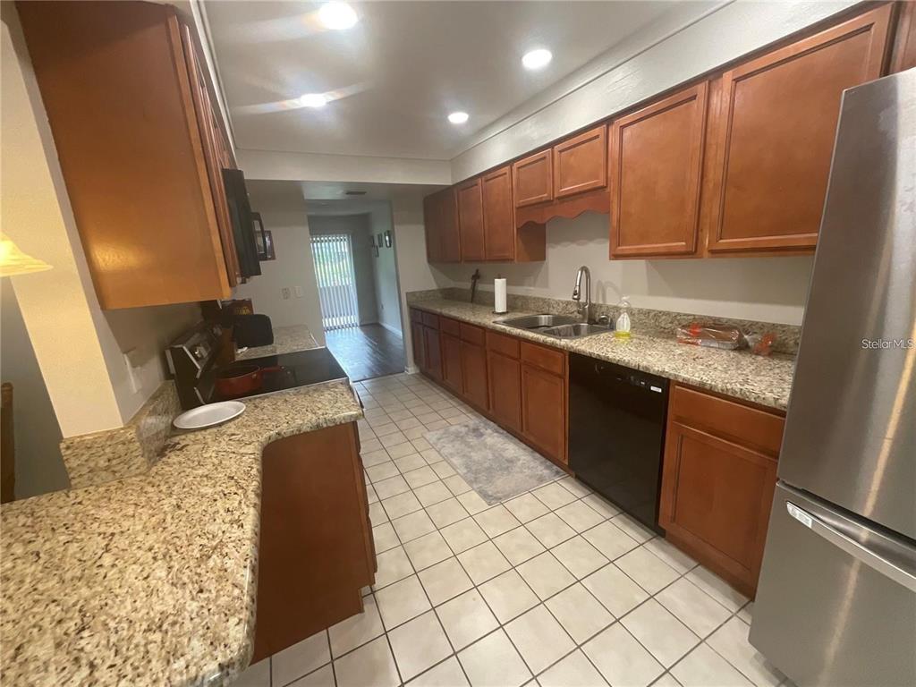 A kitchen features wood cabinets, granite countertops, tile flooring, and stainless steel appliances — 2500 21ST STREET NW UNIT 58, WINTER HAVEN, FL