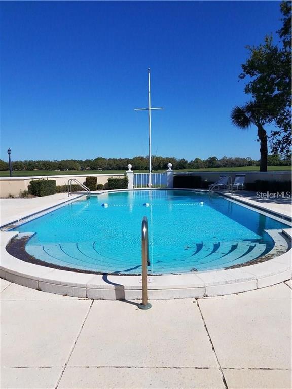 An outdoor swimming pool with a central mast feature sits on a paved patio — 51 MAC EWEN DRIVE UNIT 8, OSPREY, FL