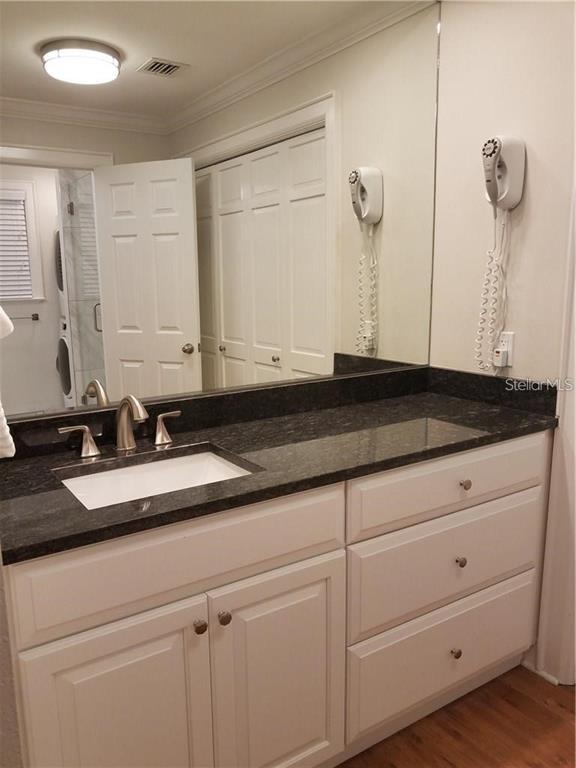 A bathroom vanity features a dark granite countertop, white cabinets, and a wall-mounted hair dryer — 51 MAC EWEN DRIVE UNIT 8, OSPREY, FL
