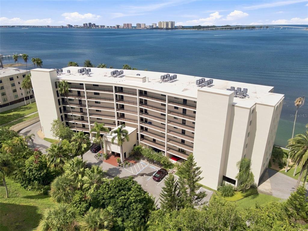 An aerial view of a multi-story apartment building situated along a waterfront with palm trees — 55 ROGERS STREET UNIT 204, CLEARWATER, FL