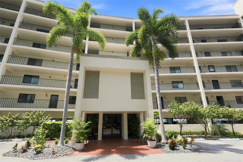 The exterior of a multi-story apartment building features a central entrance flanked by two palm trees — 55 ROGERS STREET UNIT 204, CLEARWATER, FL