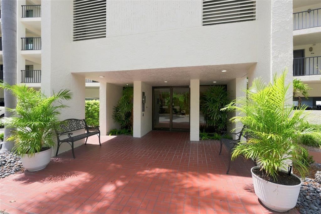 The exterior entrance of a building features a red brick patio, two benches, and plants — 55 ROGERS STREET UNIT 204, CLEARWATER, FL