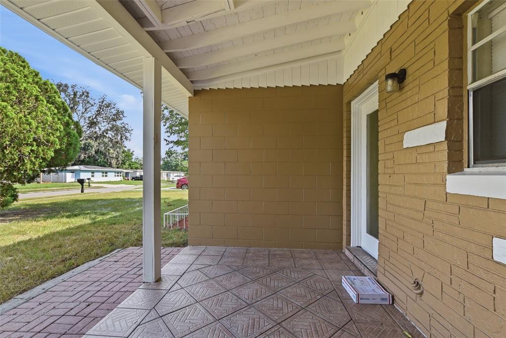A covered patio features a brick-patterned floor, a tan block wall, and a white door — 4302 MEADOWBROOK AVENUE, ORLANDO, FL