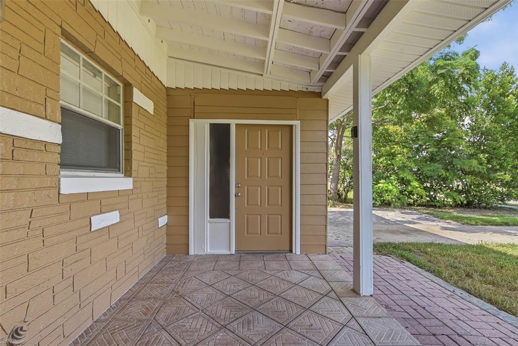 A covered front porch features a tan door, brick siding, and patterned concrete flooring — 4302 MEADOWBROOK AVENUE, ORLANDO, FL