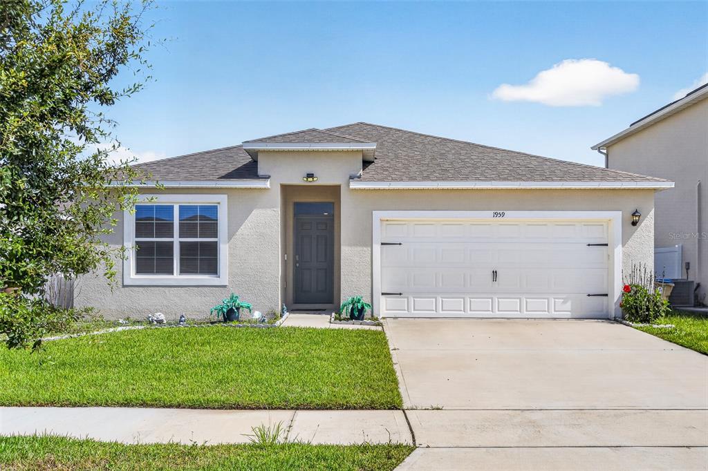 A single-story house with a white garage, gray front door, and a green lawn — 1959 CACUTTA WAY, KISSIMMEE, FL