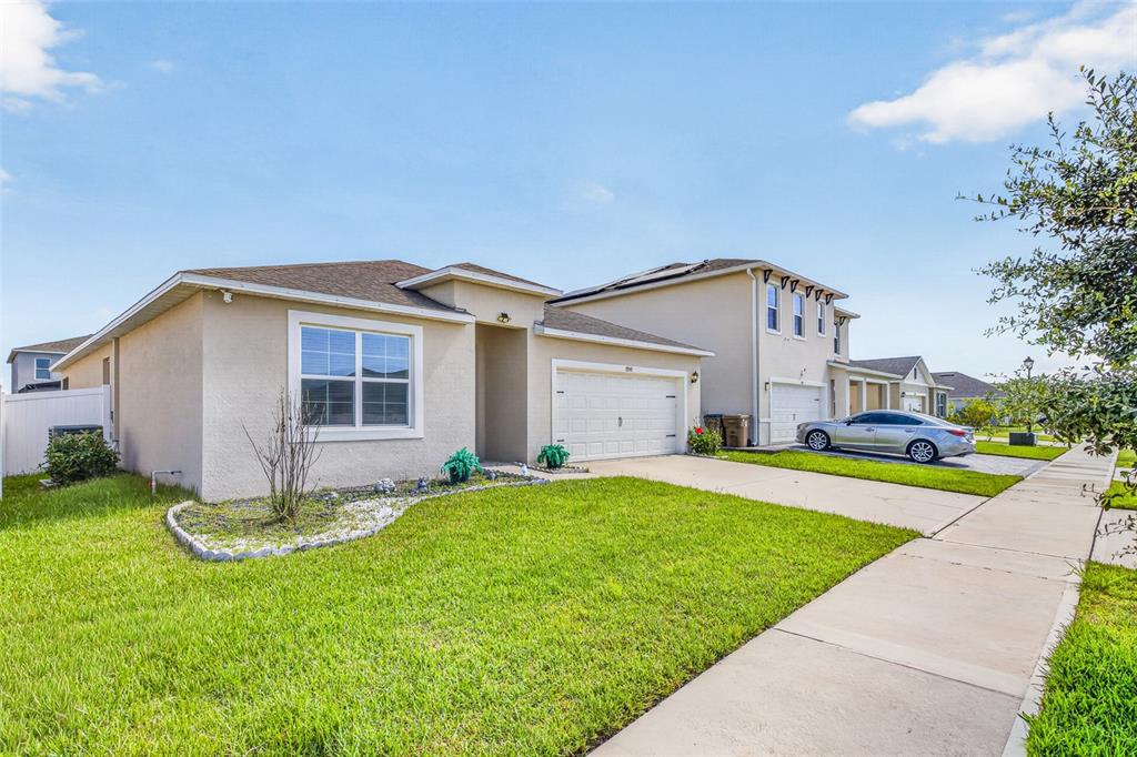 A single-story tan stucco house with a two-car garage and a front lawn — 1959 CACUTTA WAY, KISSIMMEE, FL