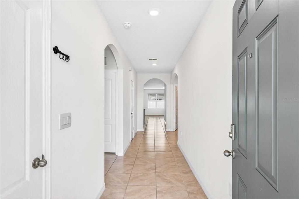 A tiled hallway leads from a gray front door toward an arched opening and window — 1959 CACUTTA WAY, KISSIMMEE, FL